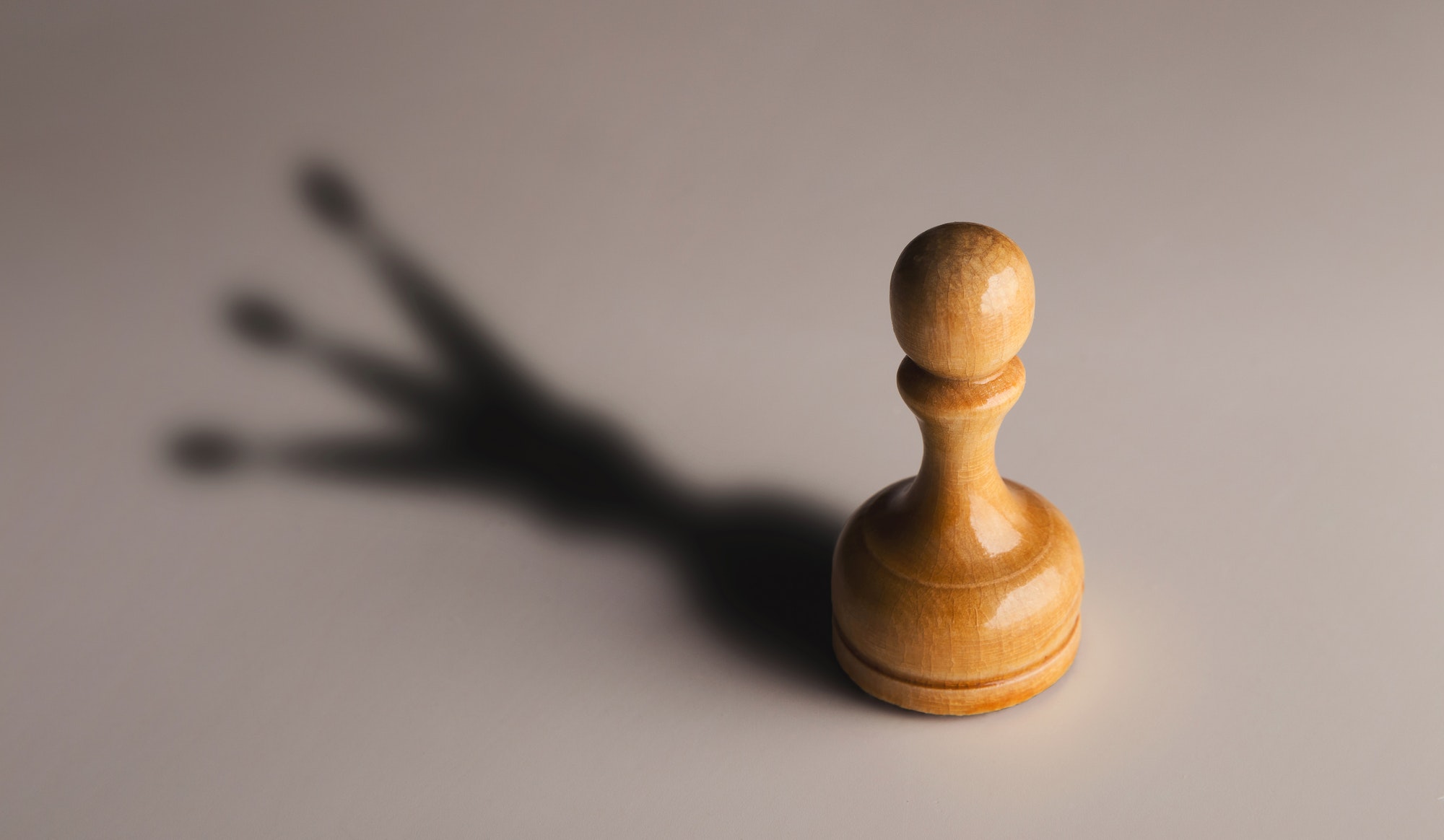 Wooden chess pawn with king shadow